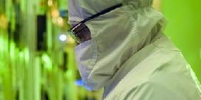 person in cleanroom wearing glasses and clean suit. Neon green background