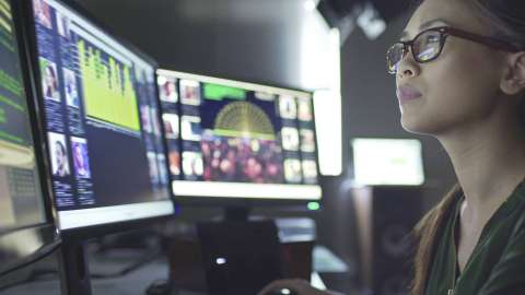 A close-up view of a person with glasses examining data and images displayed across multiple computer monitors