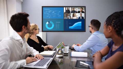 Businesspeople sitting around conference room table looking at large display