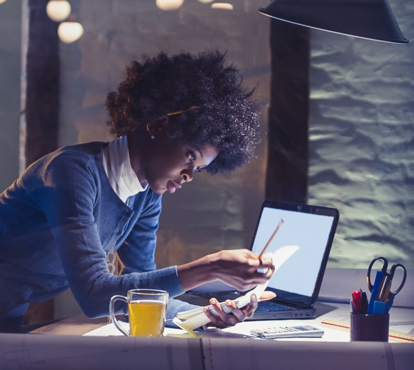 A female professional works independently in an empty office with a cup of tea and a laptop.